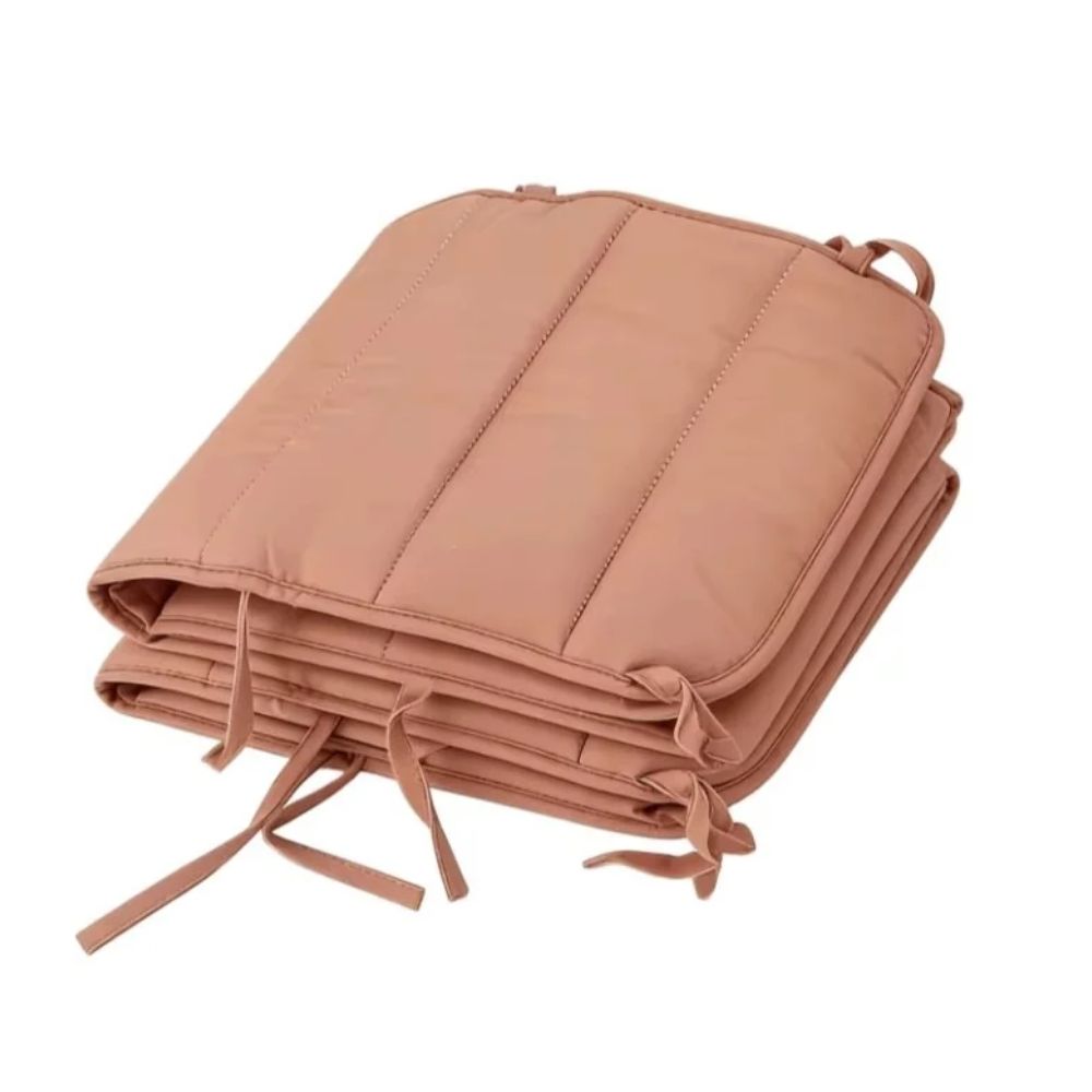 Terracotta cot bumper folded into a compact stack, showing the channel quilting and fabric ties