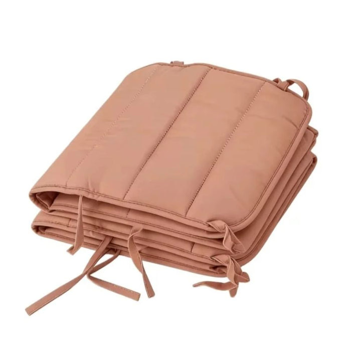 Terracotta cot bumper folded into a compact stack, showing the channel quilting and fabric ties