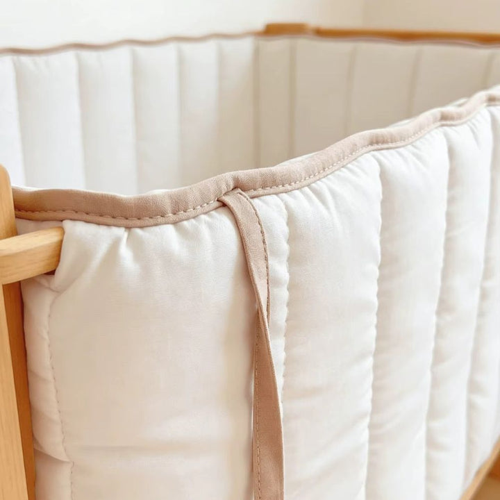 Close-up of the fabric tie and tan piping on a white quilted cot bumper
