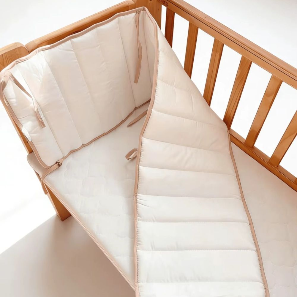 White cot bumper partly unfolded inside a timber cot, showing how it bends around the corner