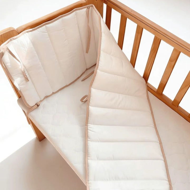 White cot bumper partly unfolded inside a timber cot, showing how it bends around the corner